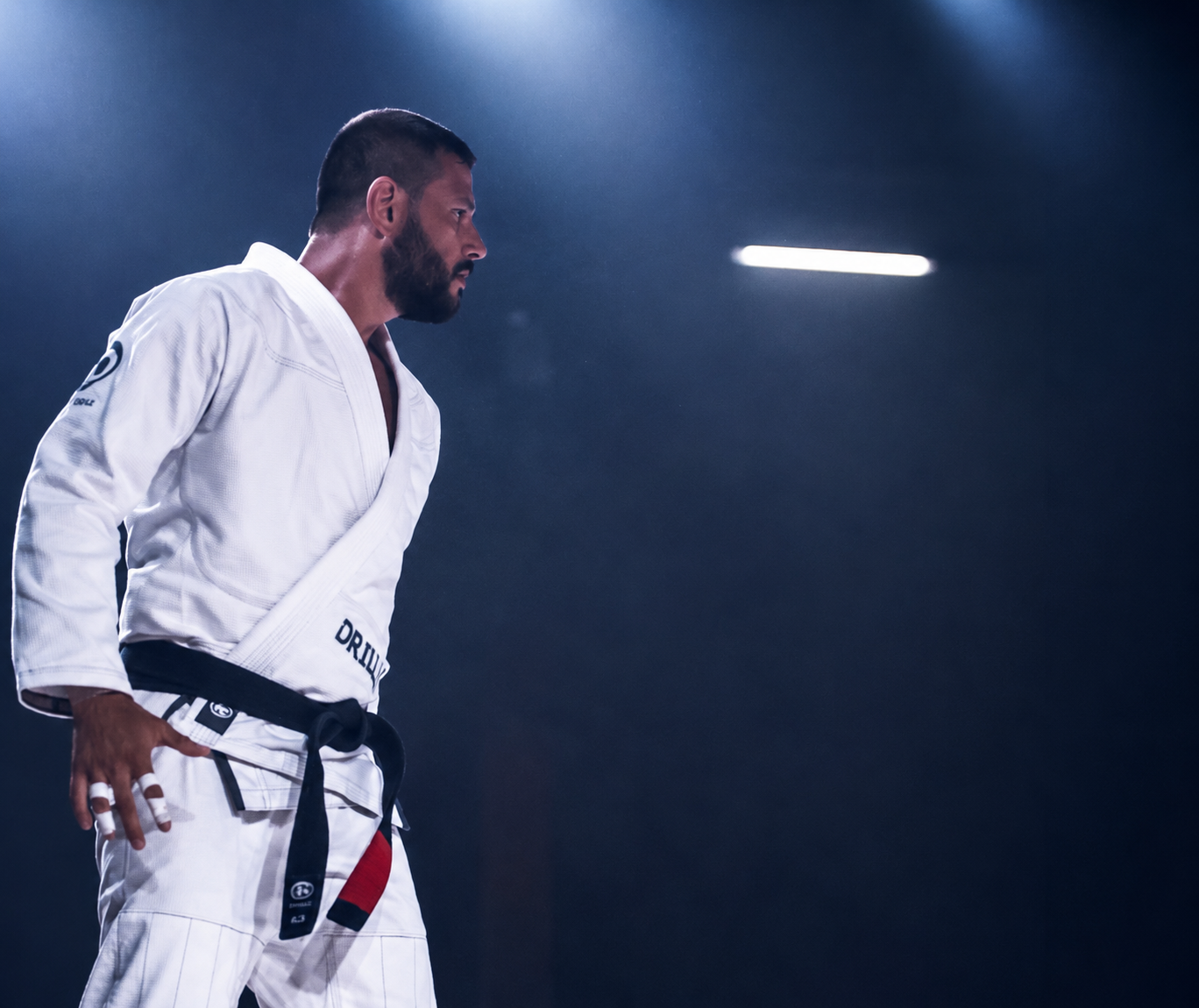 Leandro Albuquerque de kimono branco e faixa-preta, de perfil, em ambiente de competição, representando preparação e disciplina