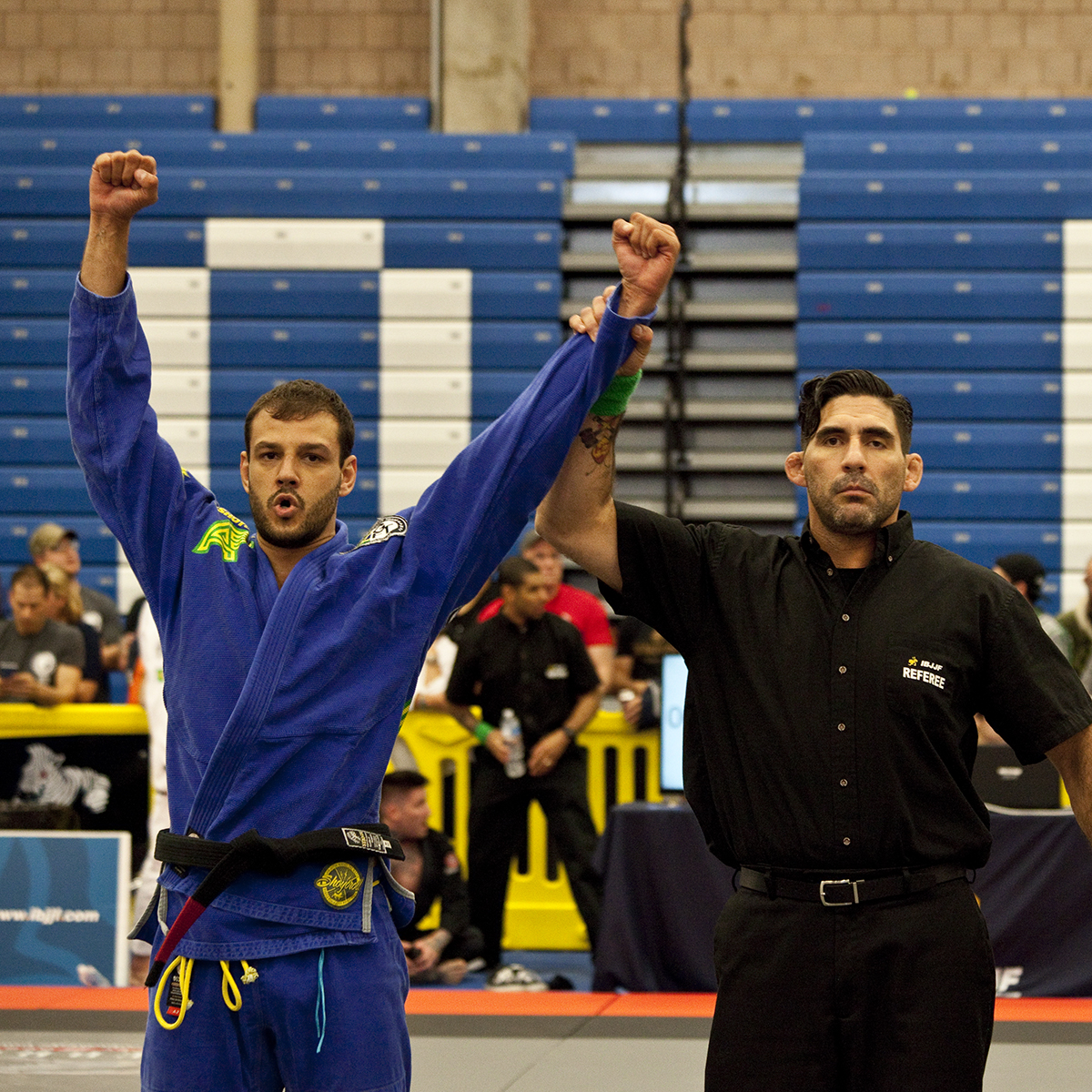 Leandro Albuquerque de kimono azul e faixa-preta tendo o braço levantado pelo árbitro após vencer uma luta de jiu-jitsu
